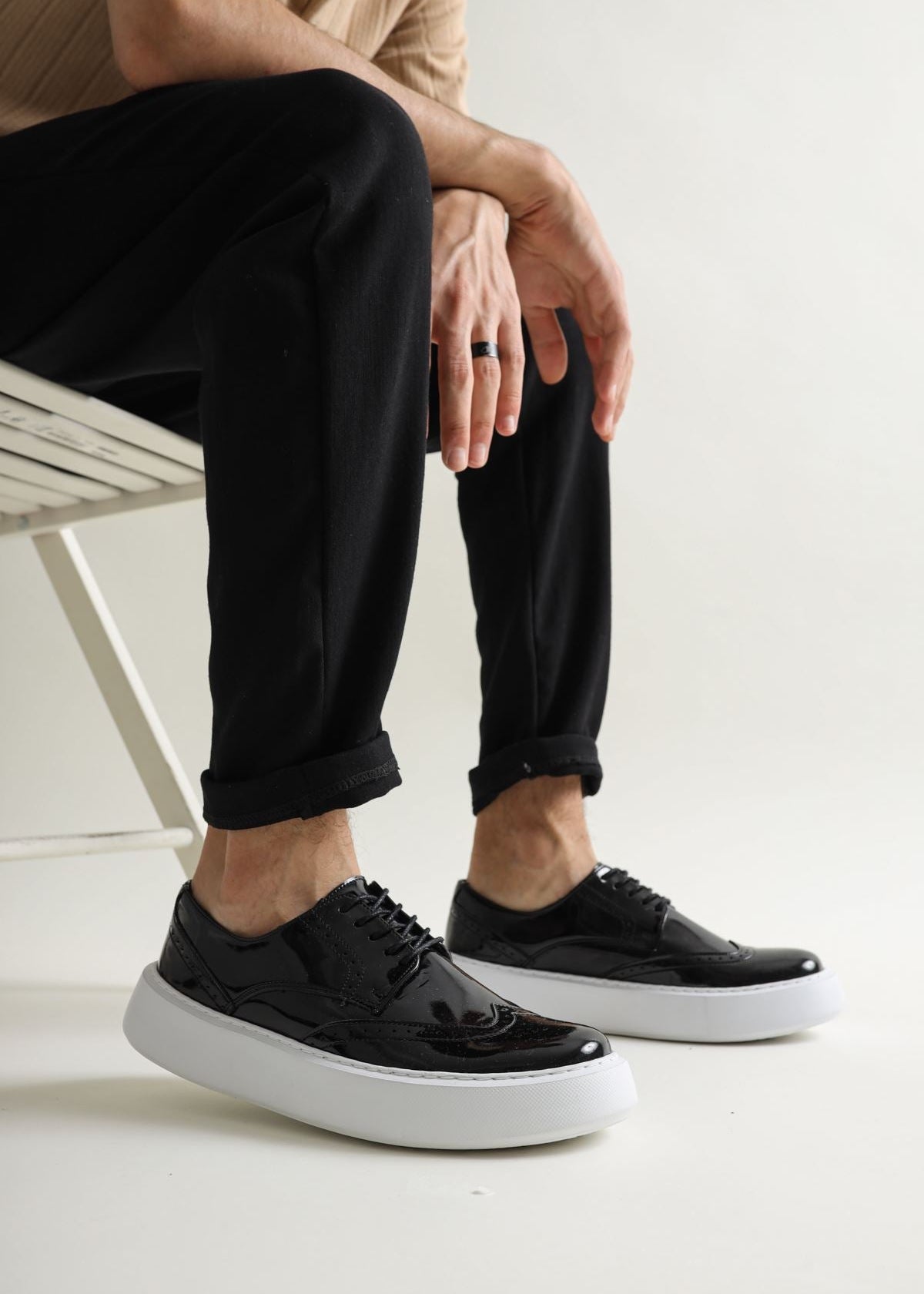 A man's foot wearing a black patent leather dress shoe with a contrasting white sole, the shoe is laced up and the person is standing on a light colored floor.